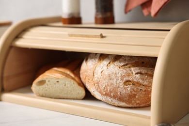 Wooden bread basket with freshly baked loaves on white marble table in kitchen, closeup