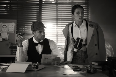 Photo of Old fashioned detective with his colleague working in office. Black and white effect