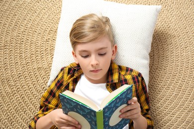 Photo of Little boy reading book on floor, top view