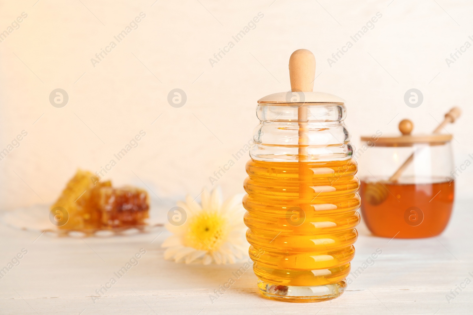 Photo of Glass jar with sweet honey on table against light background. Space for text