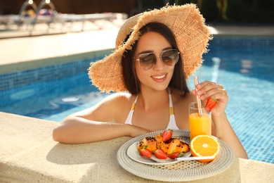 Photo of Young woman with delicious breakfast on tray in swimming pool