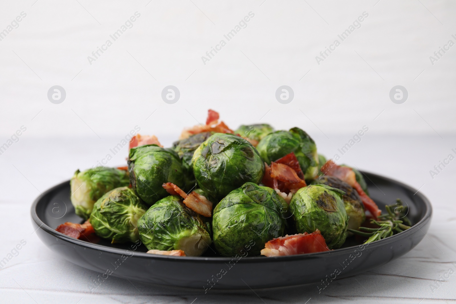 Photo of Delicious roasted Brussels sprouts, bacon and rosemary on white textured table, closeup