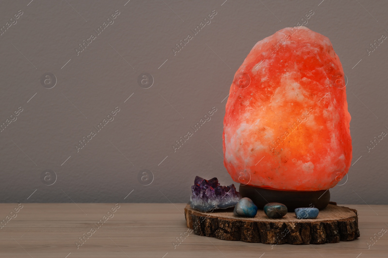 Photo of Himalayan salt lamp on wooden table near grey wall, space for text