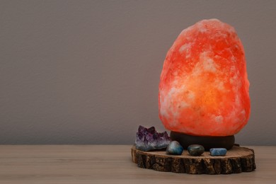 Himalayan salt lamp on wooden table near grey wall, space for text