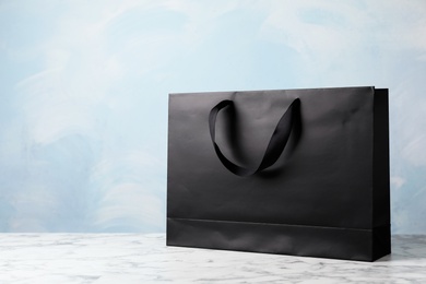 Photo of Paper shopping bag with ribbon handles on table against color background. Mockup for design