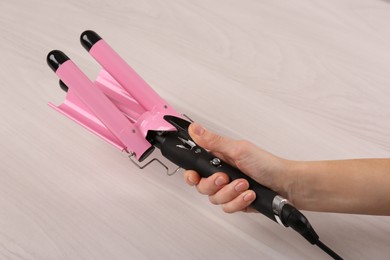 Photo of Woman holding modern triple curling iron on wooden background, closeup