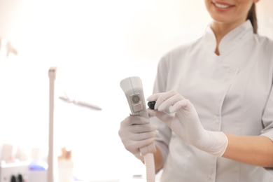 Photo of Young woman holding professional laser epilator in beauty salon, closeup