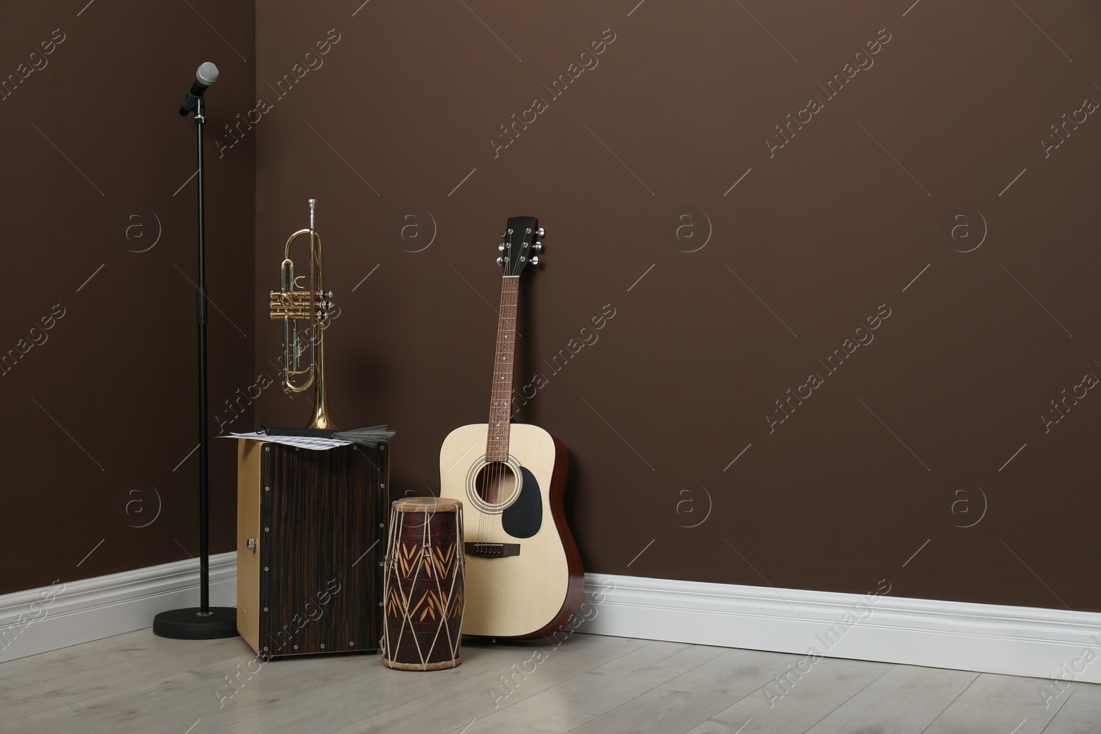 Photo of Acoustic guitar, trumpet, hand drum and microphone near brown wall indoors, space for text. Musical instruments