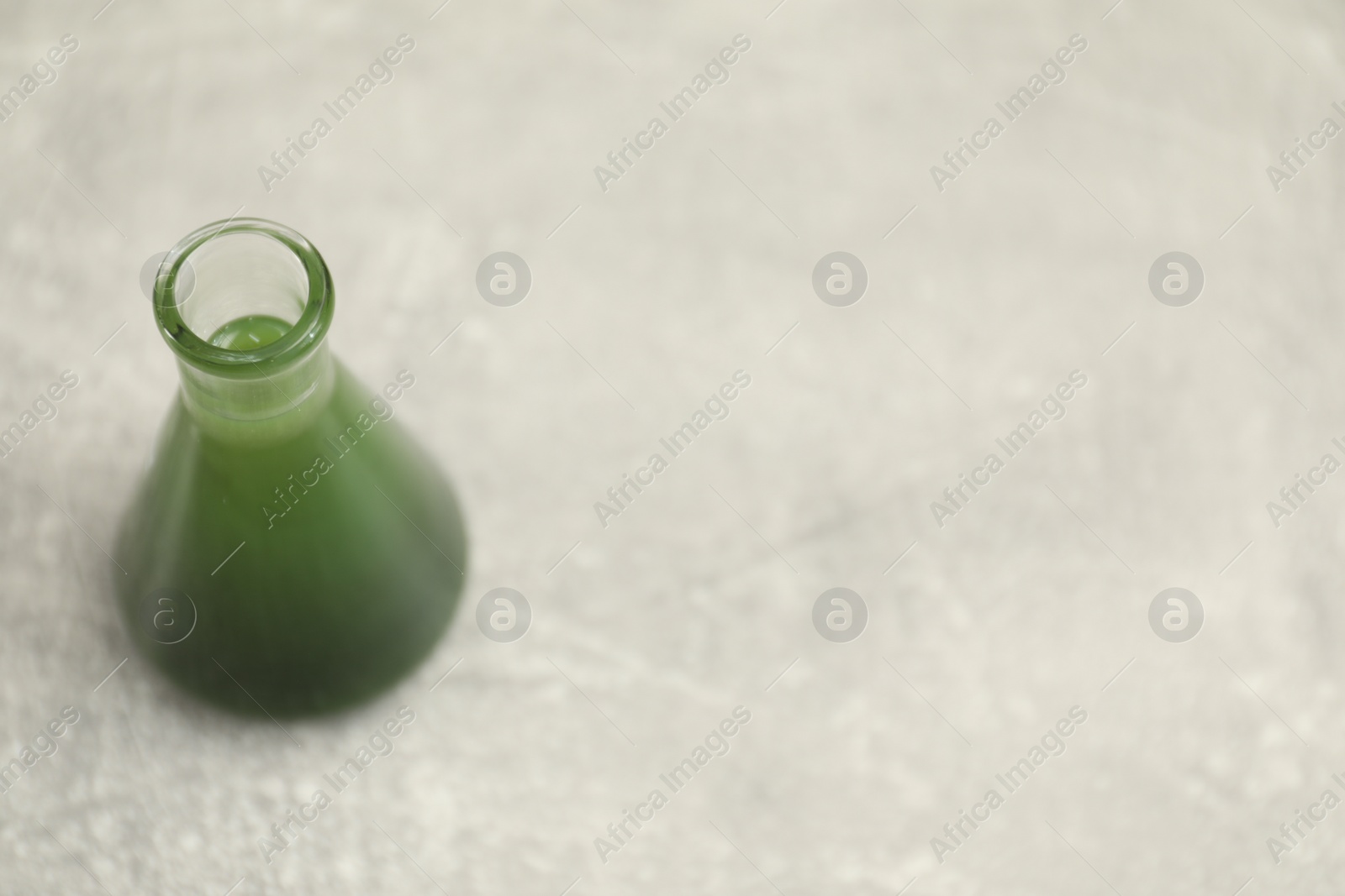 Photo of Flask with green crude oil on light grey table, space for text