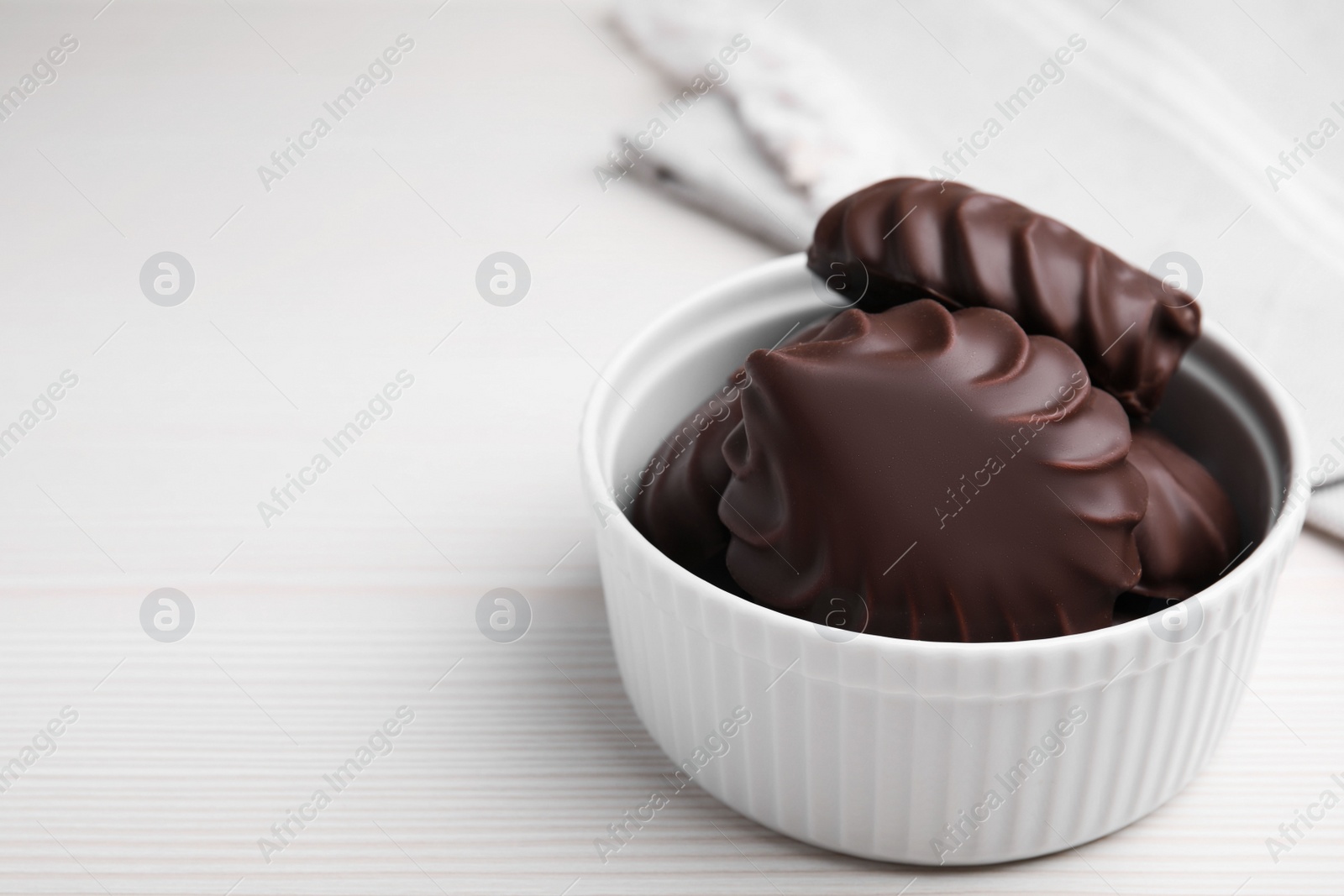 Photo of Delicious chocolate covered zephyrs in bowl on white wooden table, space for text
