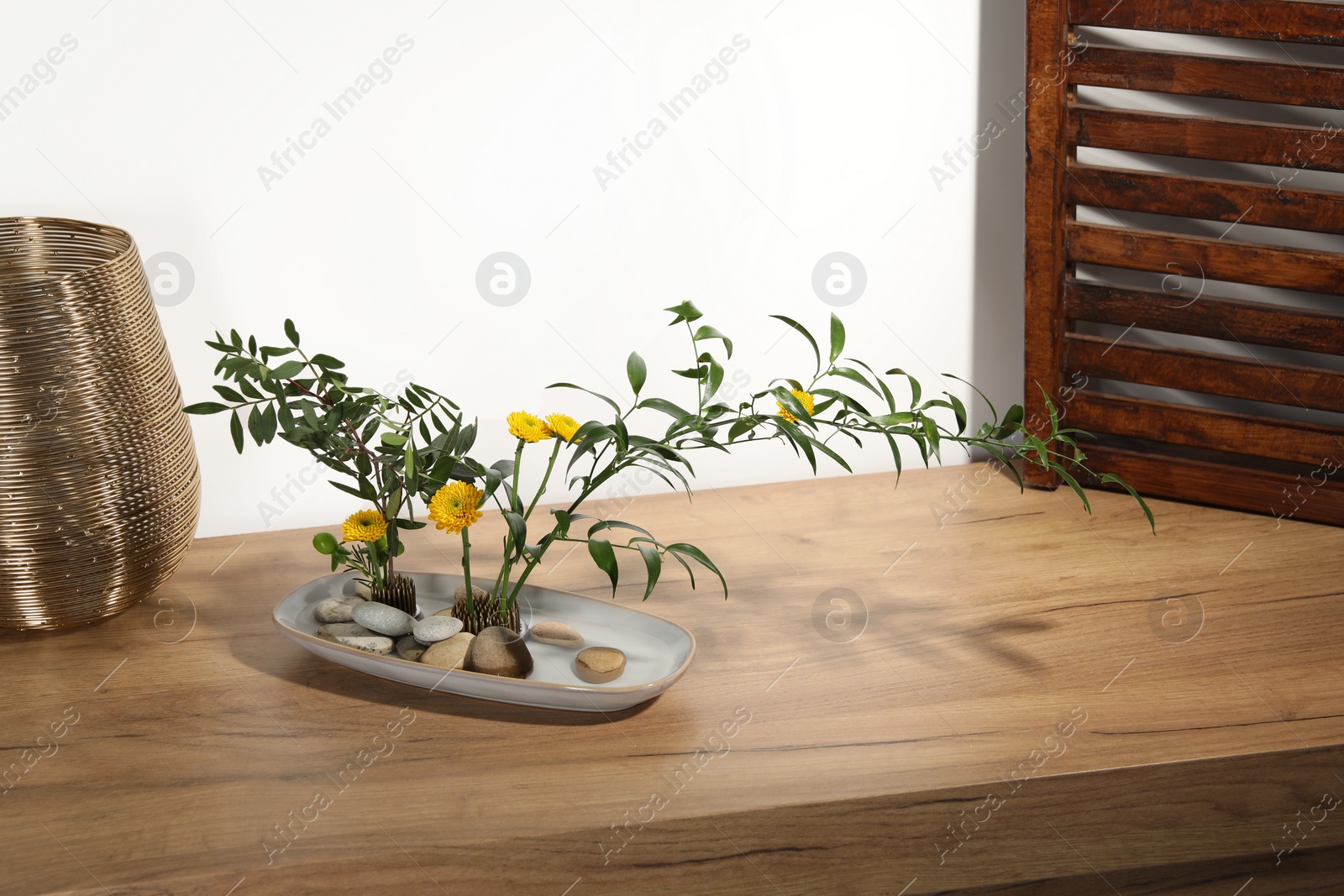 Photo of Stylish ikebana with beautiful yellow flowers and green branches carrying cozy atmosphere at home