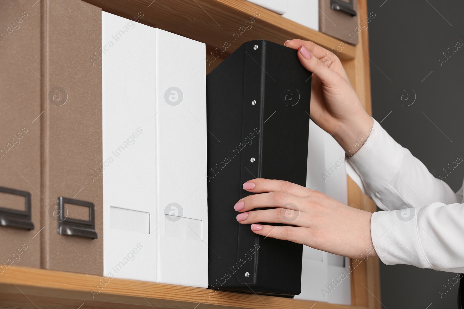 Photo of Woman taking folder with documents from shelf in office, closeup