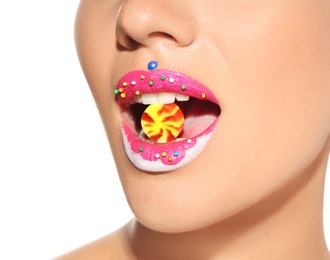 Beautiful young model with creative makeup holding candy in lips on white background