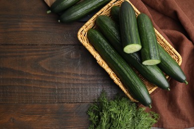 Photo of Fresh cucumbers in wicker basket and dill on wooden table, flat lay. Space for text