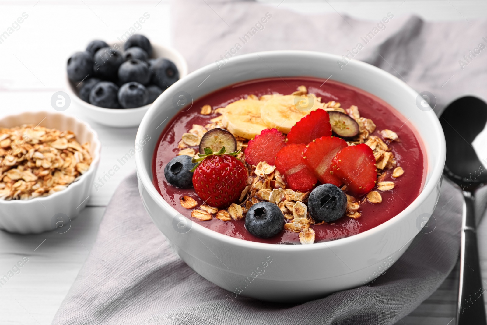 Photo of Delicious smoothie bowl with fresh berries, banana and granola on white wooden table, closeup