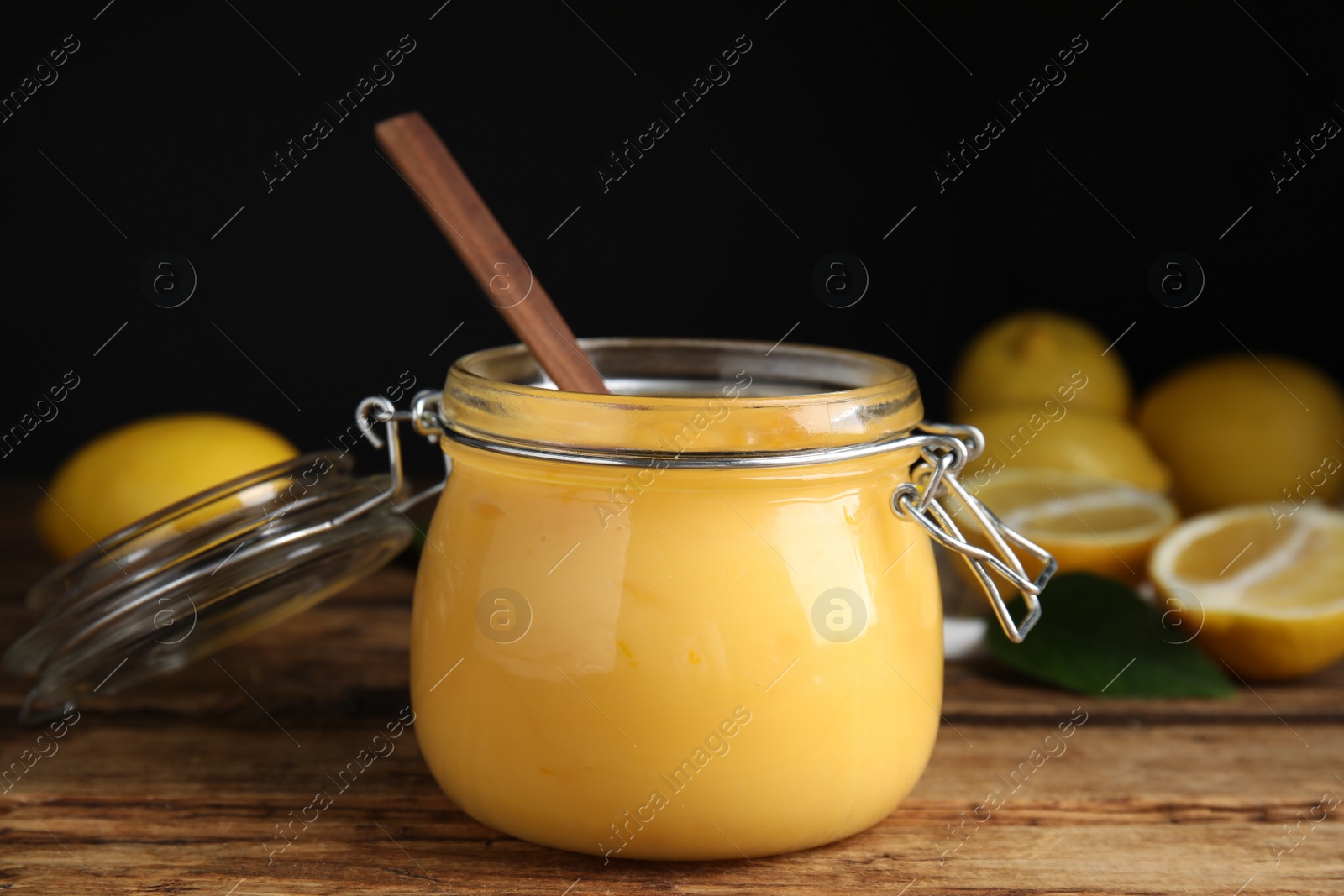 Photo of Delicious lemon curd in glass jar on wooden table