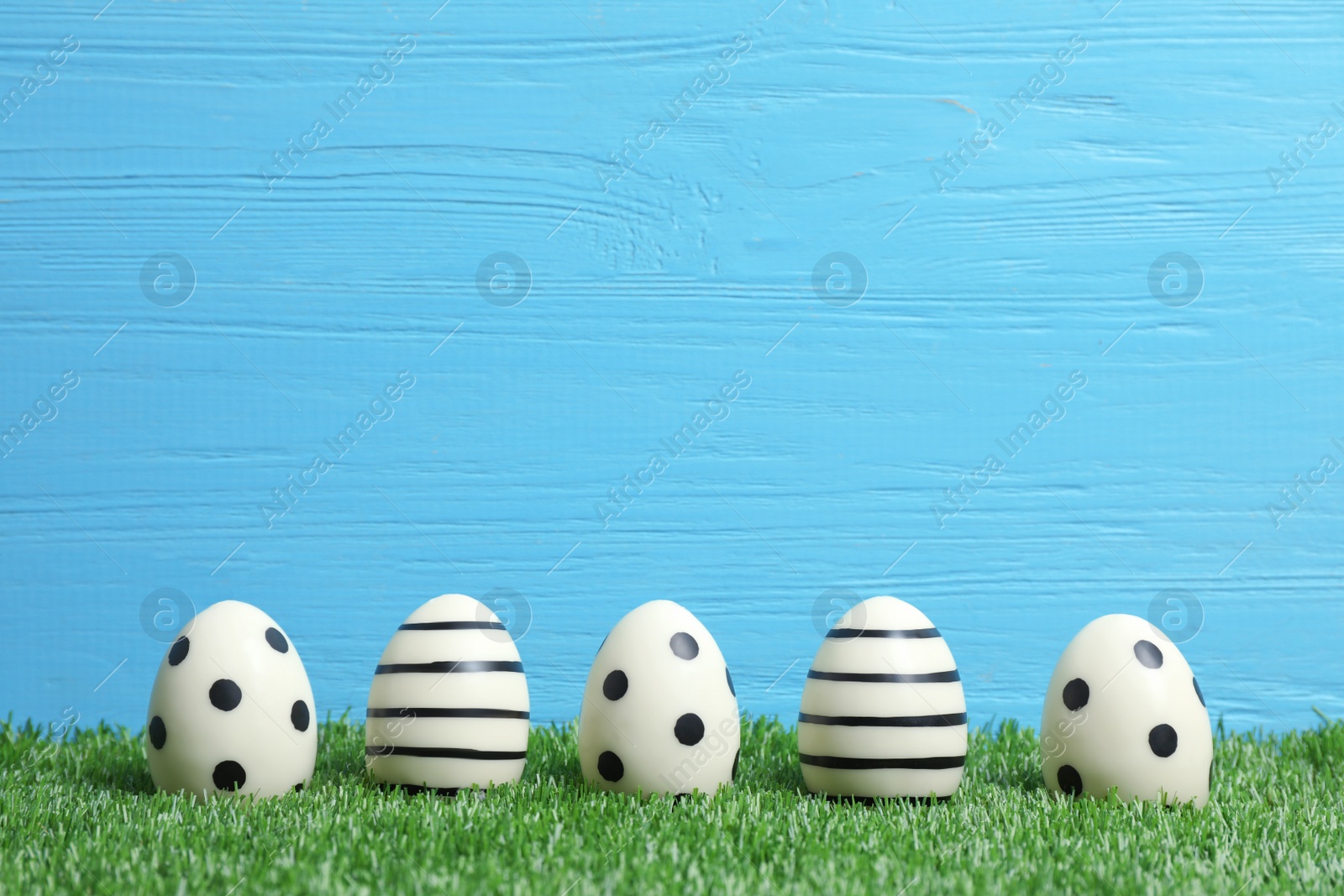 Photo of Line of traditional Easter eggs decorated with black paint on green lawn against wooden background, space for text