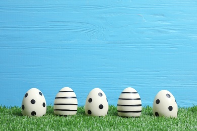 Photo of Line of traditional Easter eggs decorated with black paint on green lawn against wooden background, space for text