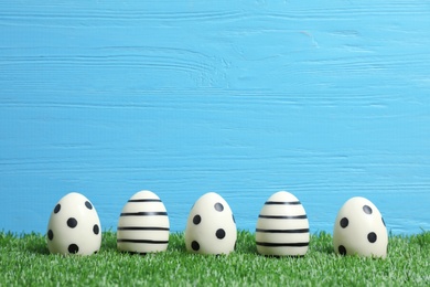 Line of traditional Easter eggs decorated with black paint on green lawn against wooden background, space for text