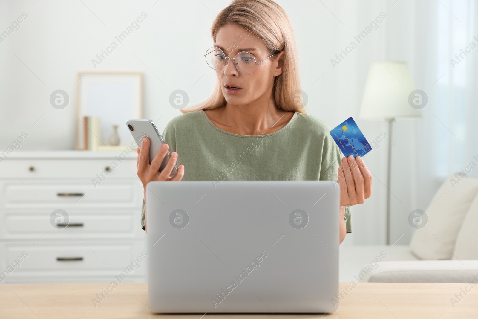 Photo of Stressed woman with credit card and smartphone using laptop at home. Be careful - fraud