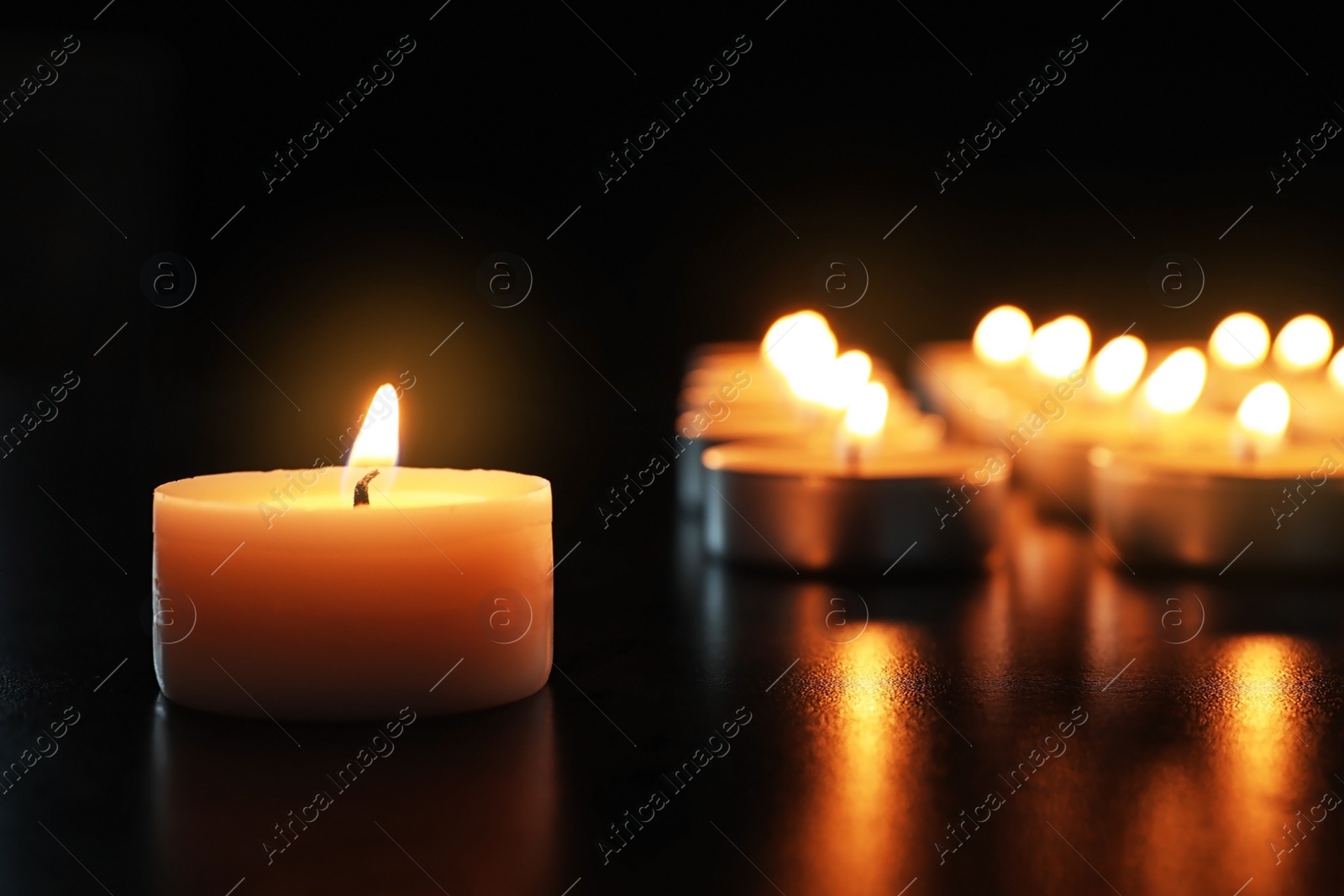 Photo of Wax candle burning on table in darkness, closeup