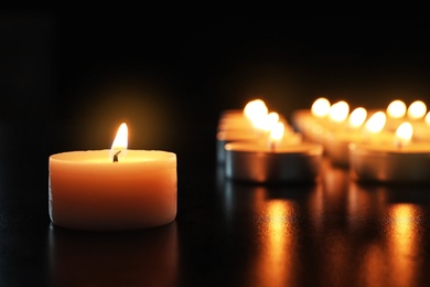 Photo of Wax candle burning on table in darkness, closeup