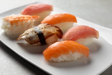 Photo of Plate with delicious nigiri sushi on grey table, closeup