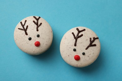 Photo of Tasty reindeer Christmas macarons on light blue background, flat lay