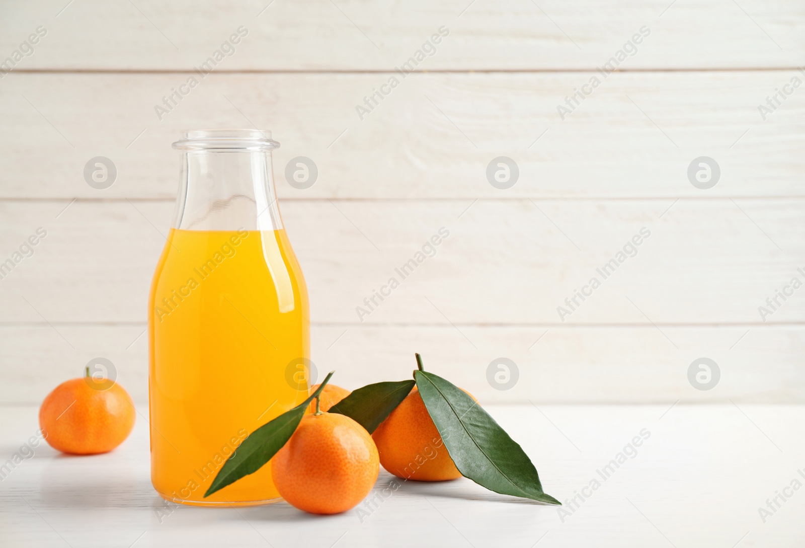 Photo of Fresh tangerines and bottle of juice on white wooden table. Space for text