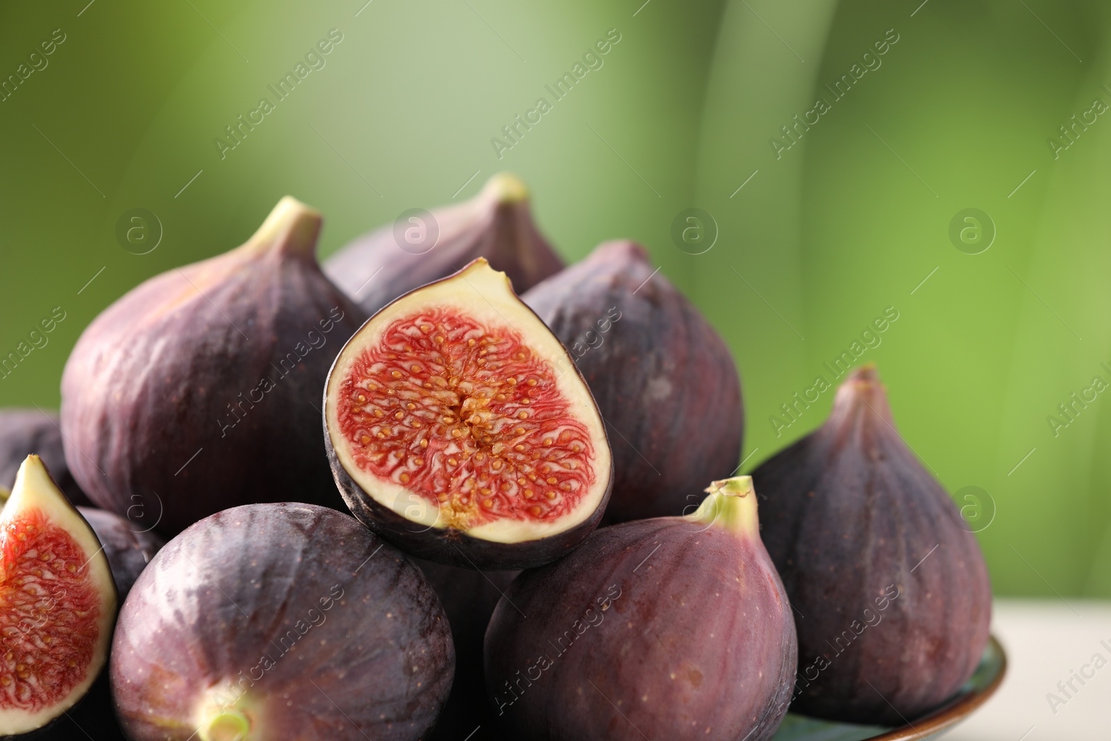 Photo of Fresh ripe figs against blurred green background, closeup