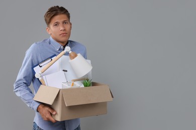 Photo of Unemployed young man with box of personal office belongings on grey background. Space for text