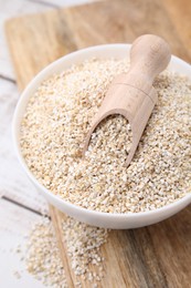 Photo of Raw barley groats and scoop in bowl on light wooden table, closeup