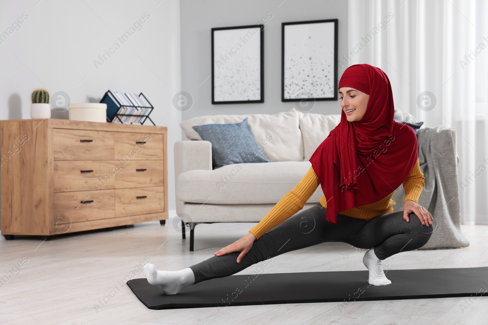 Photo of Muslim woman in hijab stretching on fitness mat at home. Space for text