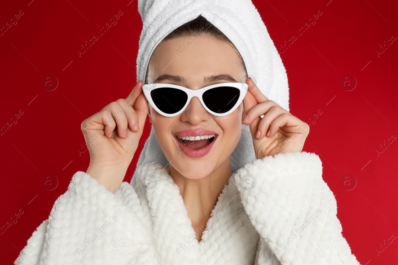 Photo of Beautiful young woman in bathrobe and sunglasses on red background