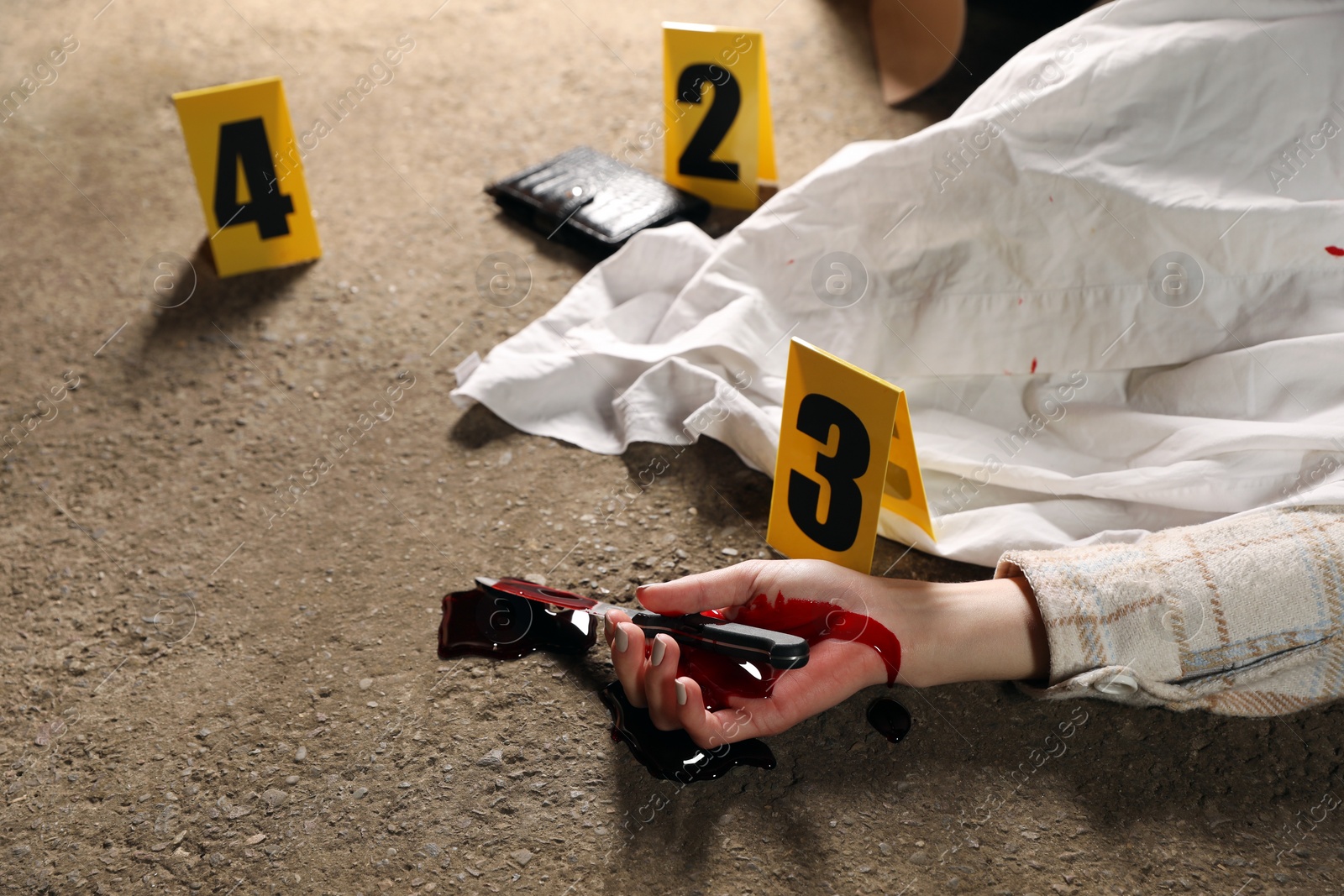 Photo of Crime scene with dead woman's body, bloody knife and markers outdoors, closeup