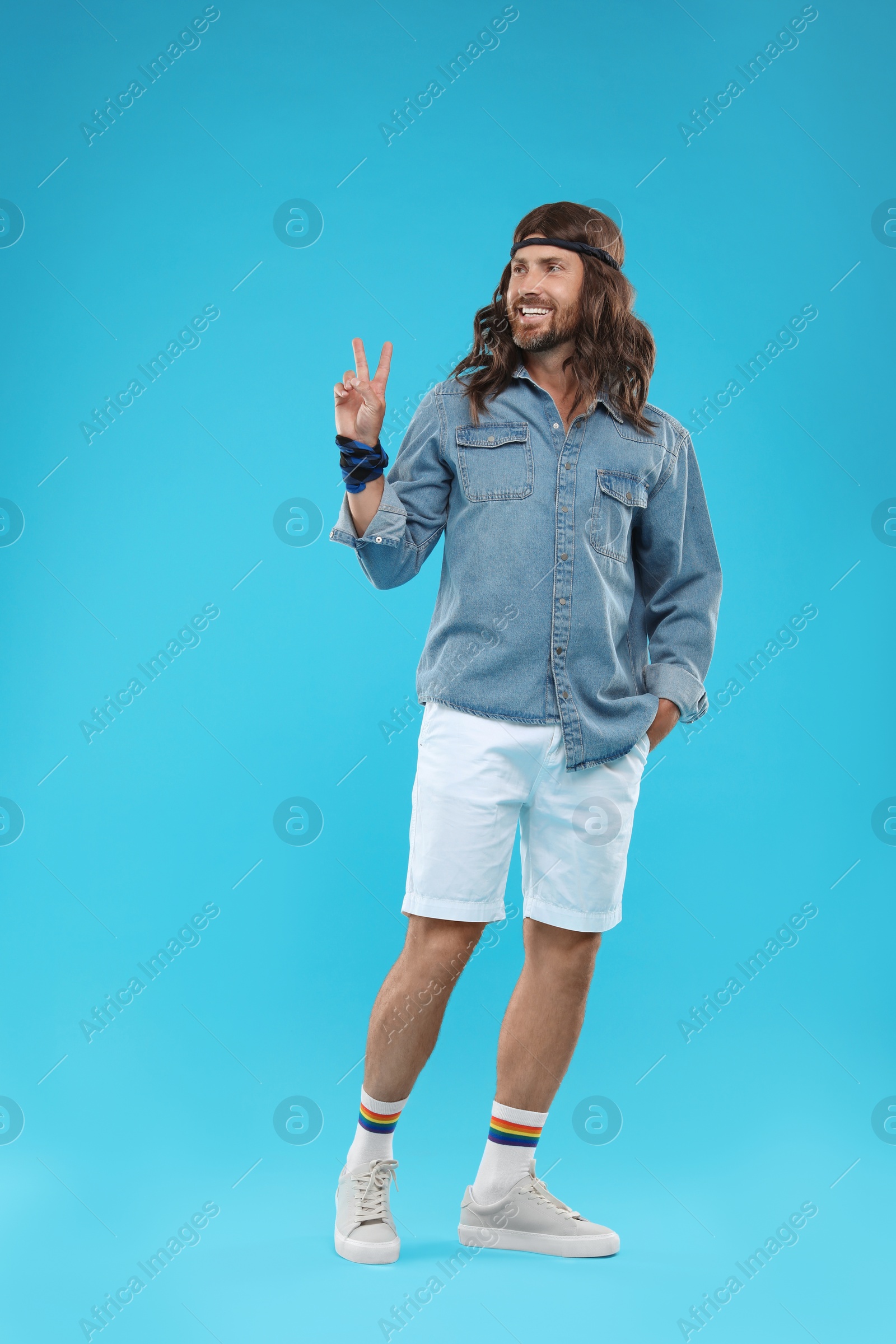 Photo of Stylish hippie man showing V-sign on light blue background