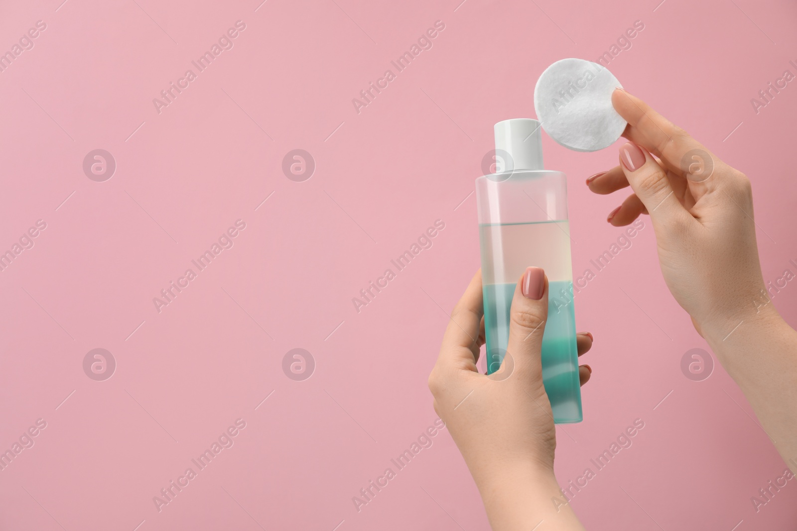 Photo of Woman holding makeup remover and cotton pad on pink background, closeup. Space for text