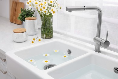 Photo of Sink with water and beautiful chamomiles indoors