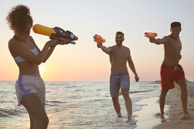 Photo of Friends with water guns having fun on beach at sunset