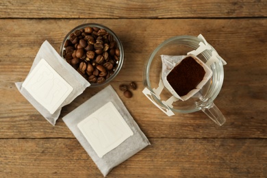 Photo of Drip coffee bags, beans and glass cup on wooden  table, flat lay
