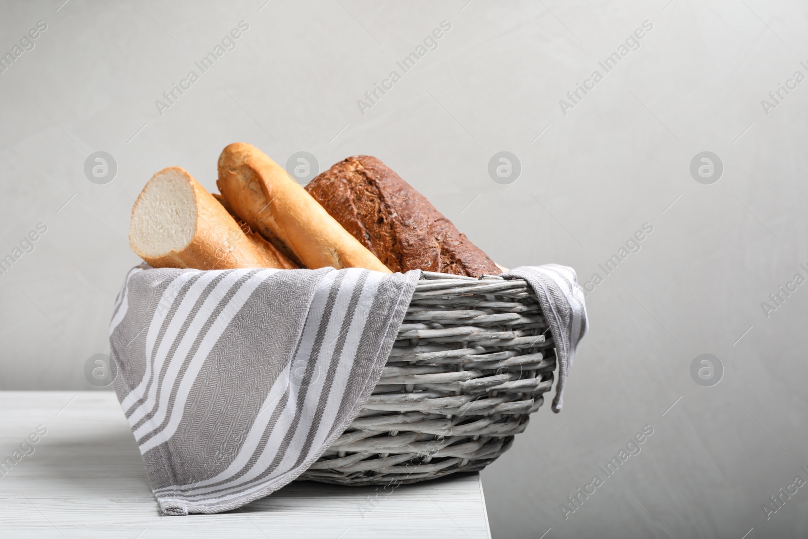 Photo of Different tasty baguettes in basket on white wooden table. Space for text