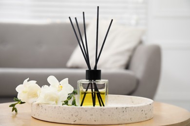 Reed diffuser with freesia on wooden table in living room
