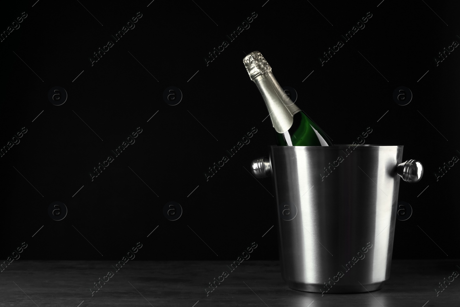 Photo of Bottle of champagne in bucket on black background. Space for text