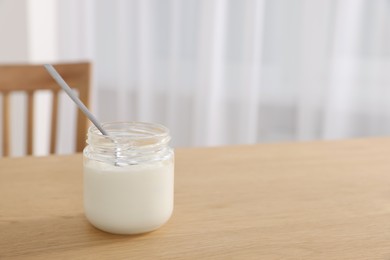 Photo of Jar of delicious yogurt with spoon on wooden table indoors. Space for text