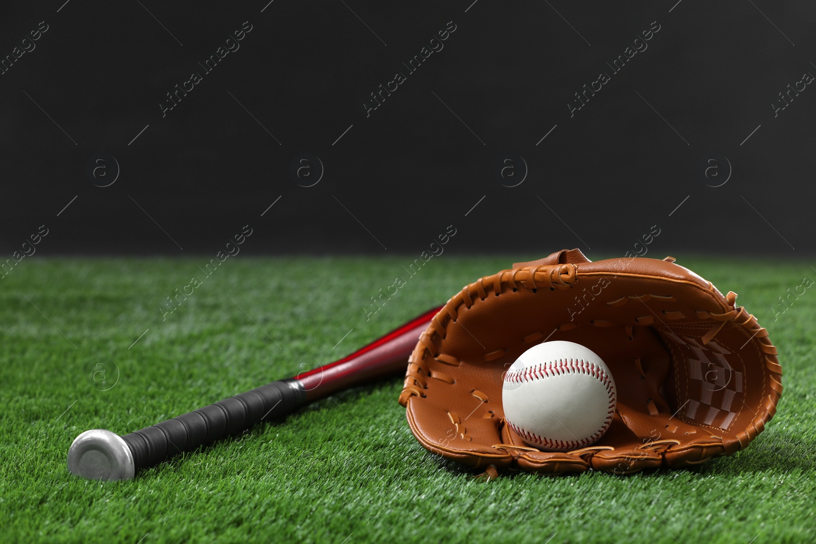 Photo of Baseball bat, leather glove and ball on green grass against dark background. Space for text