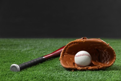 Photo of Baseball bat, leather glove and ball on green grass against dark background. Space for text