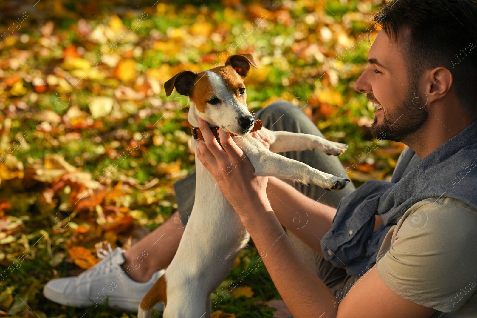 Photo of Man with adorable Jack Russell Terrier in autumn park. Dog walking