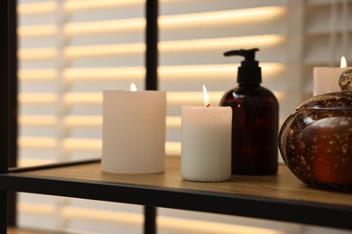 Photo of Burning candles and personal care products on shelf indoors