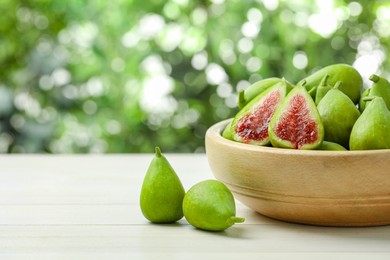 Photo of Cut and whole fresh green figs on white wooden table against blurred background, space for text