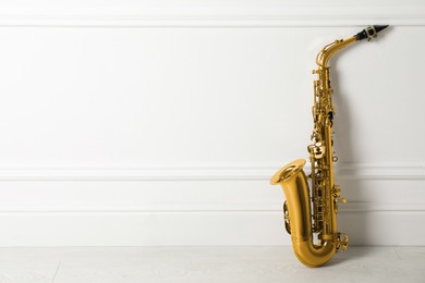 Photo of Beautiful saxophone on floor near white wall indoors, space for text